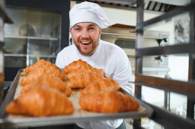 Baker holding tepsi ile ekmek fırınları taze pişmiş kruvasanlar gülümseyen.