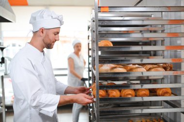Baker holding tepsi ile ekmek fırınları taze pişmiş kruvasanlar gülümseyen.