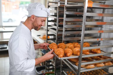 Baker holding tepsi ile ekmek fırınları taze pişmiş kruvasanlar gülümseyen.