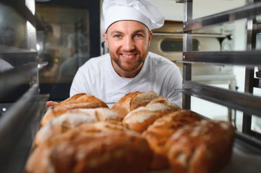 Erkek fırıncı dükkânda taze ekmek çeşitleriyle pano tutuyor..