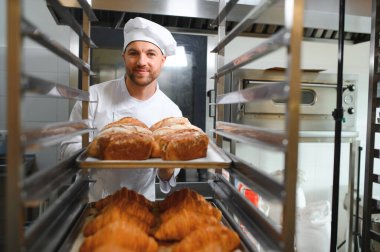 Erkek fırıncı dükkânda taze ekmek çeşitleriyle pano tutuyor..