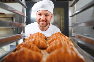 Baker holding tepsi ile ekmek fırınları taze pişmiş kruvasanlar gülümseyen.