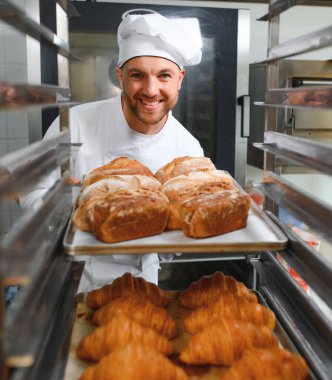 Baker holding tepsi ile ekmek fırınları taze pişmiş kruvasanlar gülümseyen.