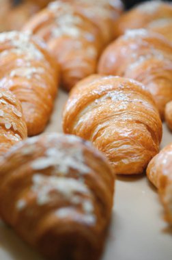 Pastanenin vitrininde çeşitli taze hamur işleri var. Rafta satılık büyük bir kruvasan var. Dükkan vitrinindeki kafede iştah açıcı altın kruvasanları yakın..
