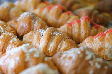 Pastanenin vitrininde çeşitli taze hamur işleri var. Rafta satılık büyük bir kruvasan var. Dükkan vitrinindeki kafede iştah açıcı altın kruvasanları yakın..