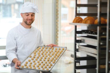 Genç fırıncı elinde taze kurabiyelerle dolu bir tepsi tutuyor..