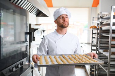 Genç fırıncı elinde taze kurabiyelerle dolu bir tepsi tutuyor..