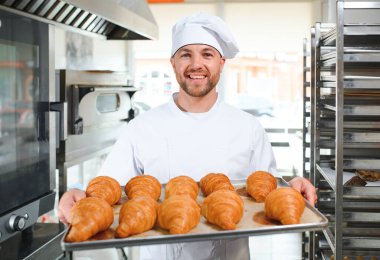 Üretim, taze pişmiş kruvasanlar dolu üniforma holding tepsisinde yakışıklı baker.