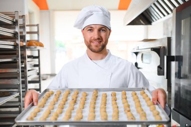 İş yerindeki genç beyaz işçi kurabiye tepsisi takıyor..