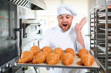 Üretim, taze pişmiş kruvasanlar dolu üniforma holding tepsisinde yakışıklı baker.