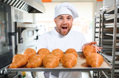 Genç, yakışıklı bir fırıncı elinde Fransız kruvasanı ile bir tepsi tutuyor ve gülümsüyor..