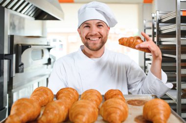 Genç, yakışıklı bir fırıncı elinde Fransız kruvasanı ile bir tepsi tutuyor ve gülümsüyor..