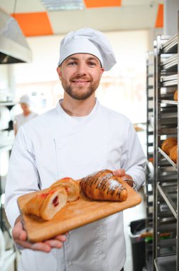 Üretim, taze pişmiş kruvasanlar dolu üniforma holding tepsisinde yakışıklı baker.