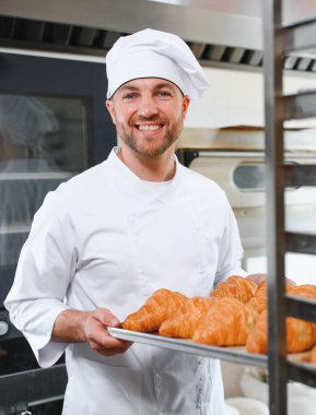 Üretim, taze pişmiş kruvasanlar dolu üniforma holding tepsisinde yakışıklı baker.