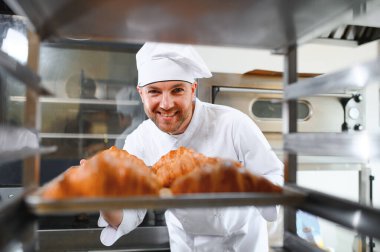 Genç, yakışıklı bir fırıncı elinde Fransız kruvasanı ile bir tepsi tutuyor ve gülümsüyor..