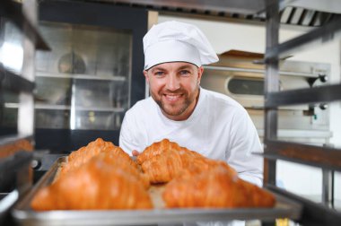 Üretim, taze pişmiş kruvasanlar dolu üniforma holding tepsisinde yakışıklı baker.