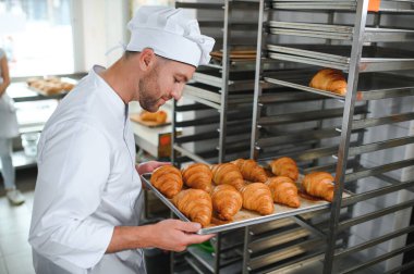 Üretim, taze pişmiş kruvasanlar dolu üniforma holding tepsisinde yakışıklı baker.