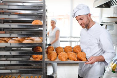 Üretim, taze pişmiş kruvasanlar dolu üniforma holding tepsisinde yakışıklı baker.