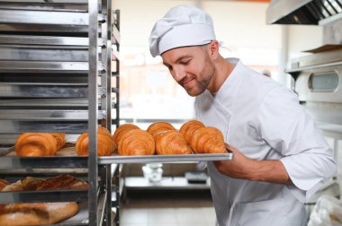 Baker holding tepsi ile ekmek fırınları taze pişmiş kruvasanlar gülümseyen.