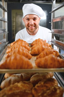 Üretim, taze pişmiş kruvasanlar dolu üniforma holding tepsisinde yakışıklı baker.