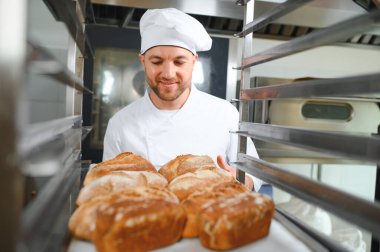 Erkek fırıncı dükkânda taze ekmek çeşitleriyle pano tutuyor..