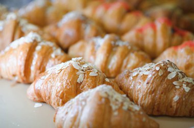 Pastanenin vitrininde çeşitli taze hamur işleri var. Rafta satılık büyük bir kruvasan var. Dükkan vitrinindeki kafede iştah açıcı altın kruvasanları yakın..