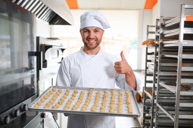 Genç fırıncı elinde taze kurabiyelerle dolu bir tepsi tutuyor..
