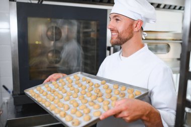 İş yerindeki genç beyaz işçi kurabiye tepsisi takıyor..