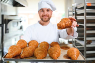 Baker holding tepsi ile ekmek fırınları taze pişmiş kruvasanlar gülümseyen.