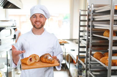 Baker holding tepsi ile ekmek fırınları taze pişmiş kruvasanlar gülümseyen.