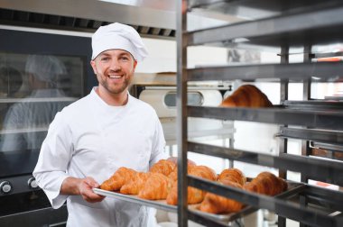 Baker holding tepsi ile ekmek fırınları taze pişmiş kruvasanlar gülümseyen.