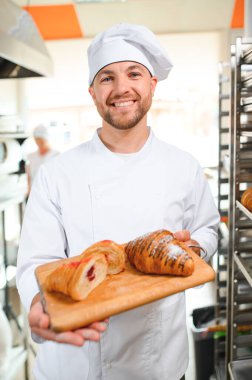 Baker holding tepsi ile ekmek fırınları taze pişmiş kruvasanlar gülümseyen.