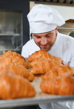 Genç, yakışıklı bir fırıncı elinde Fransız kruvasanı ile bir tepsi tutuyor ve gülümsüyor..