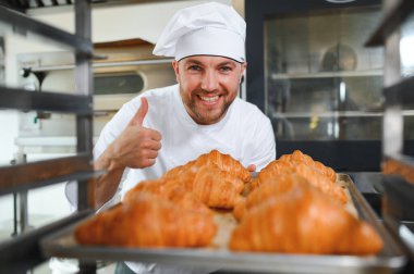 Üretim, taze pişmiş kruvasanlar dolu üniforma holding tepsisinde yakışıklı baker.