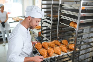 Baker holding tepsi ile ekmek fırınları taze pişmiş kruvasanlar gülümseyen.