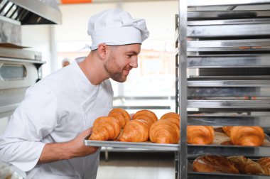 Fırının mutfağında elinde kruvasan tepsileri tutan fırıncı..