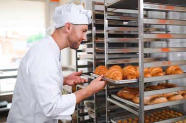 Baker holding tepsi ile ekmek fırınları taze pişmiş kruvasanlar gülümseyen.