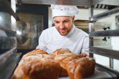 Erkek fırıncı dükkânda taze ekmek çeşitleriyle pano tutuyor..