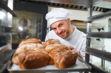 Erkek fırıncı dükkânda taze ekmek çeşitleriyle pano tutuyor..