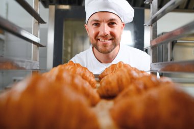 Baker holding tepsi ile ekmek fırınları taze pişmiş kruvasanlar gülümseyen.