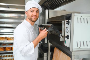 Yakışıklı baker ekmek ekmek ve fırın arka planda portresi.