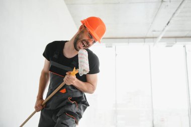 Komik ve neşeli işçi duvarları boyamak için bir silindir içinde şarkı söylüyor..