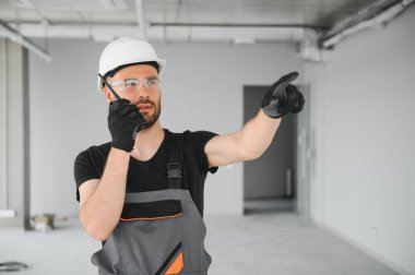 Foreman güvenlik kaskı takıyor ve inşaat alanındaki ekiple iletişim kurmak için telsiz kullanıyor..