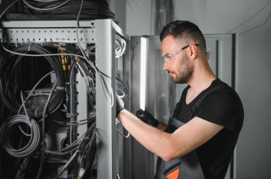 Bir teknisyen veri merkezinde sunucu ekipmanlarıyla çalışıyor. Bir adam sunucu odasında kabloları değiştiriyor..