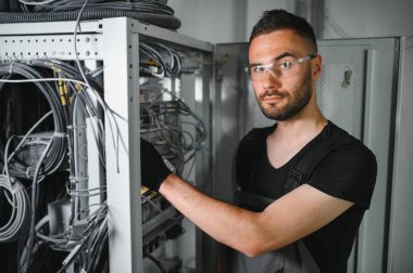 Genç adam sunucu odasında internet ekipmanı ve kablolarıyla çalışıyor..