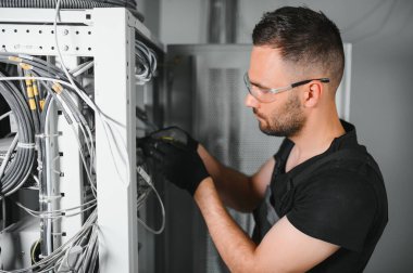 Genç adam sunucu odasında internet ekipmanı ve kablolarıyla çalışıyor..