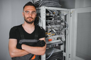 Genç adam sunucu odasında internet ekipmanı ve kablolarıyla çalışıyor..