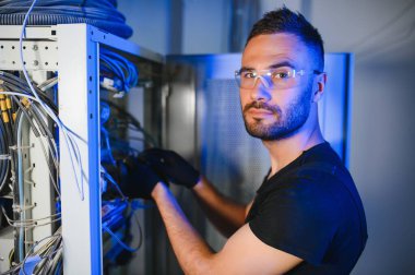 Bir teknisyen veri merkezinde sunucu ekipmanlarıyla çalışıyor. Bir adam sunucu odasında kabloları değiştiriyor..