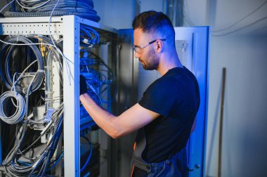 Bir teknisyen veri merkezinde sunucu ekipmanlarıyla çalışıyor. Bir adam sunucu odasında kabloları değiştiriyor..