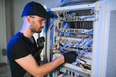 Genç adam sunucu odasında internet ekipmanı ve kablolarıyla çalışıyor..